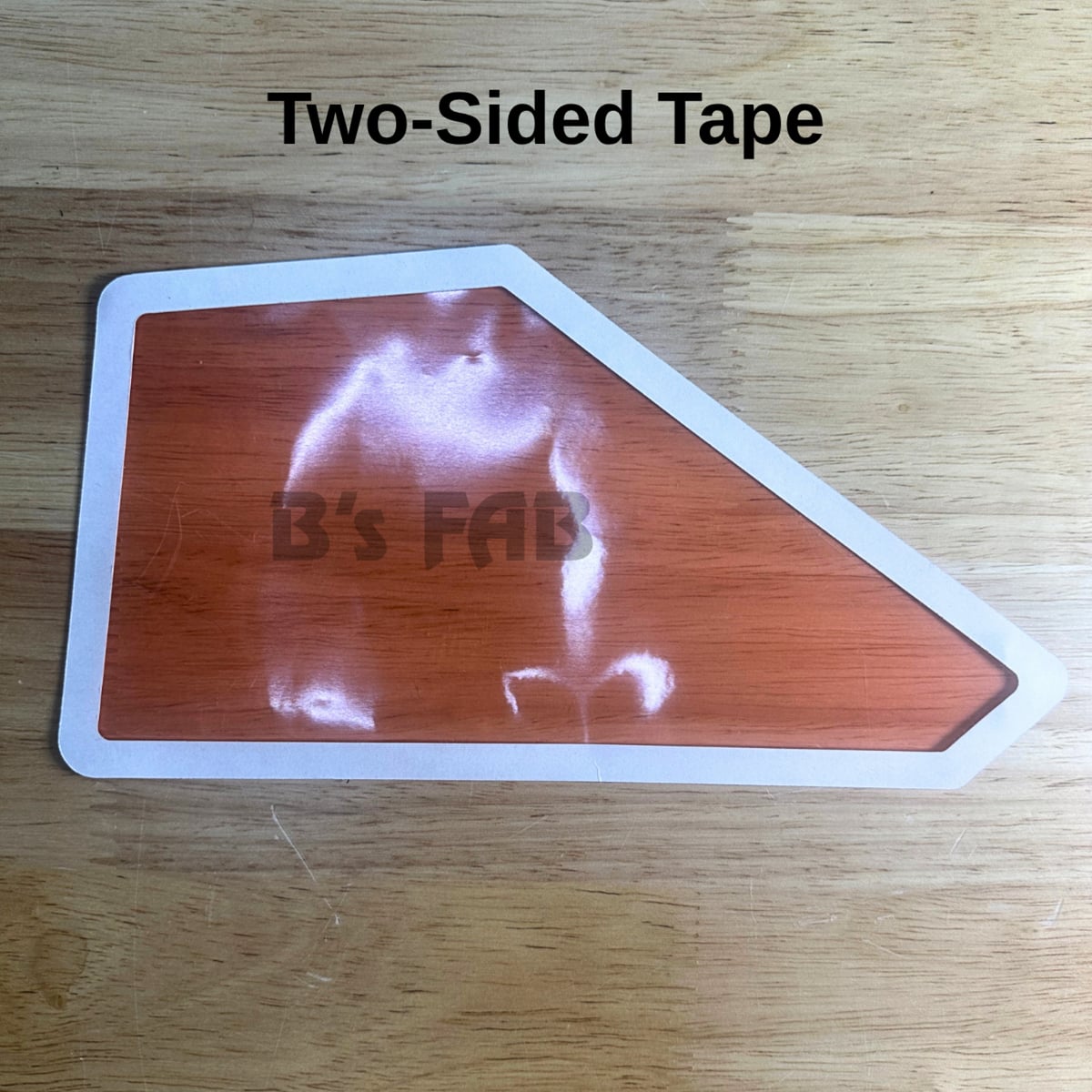 Orange irregular-shaped two-sided tape on wood surface.